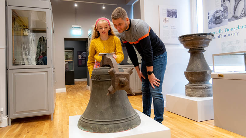 Man and young child looking at a large bell on display at Limerick Museum